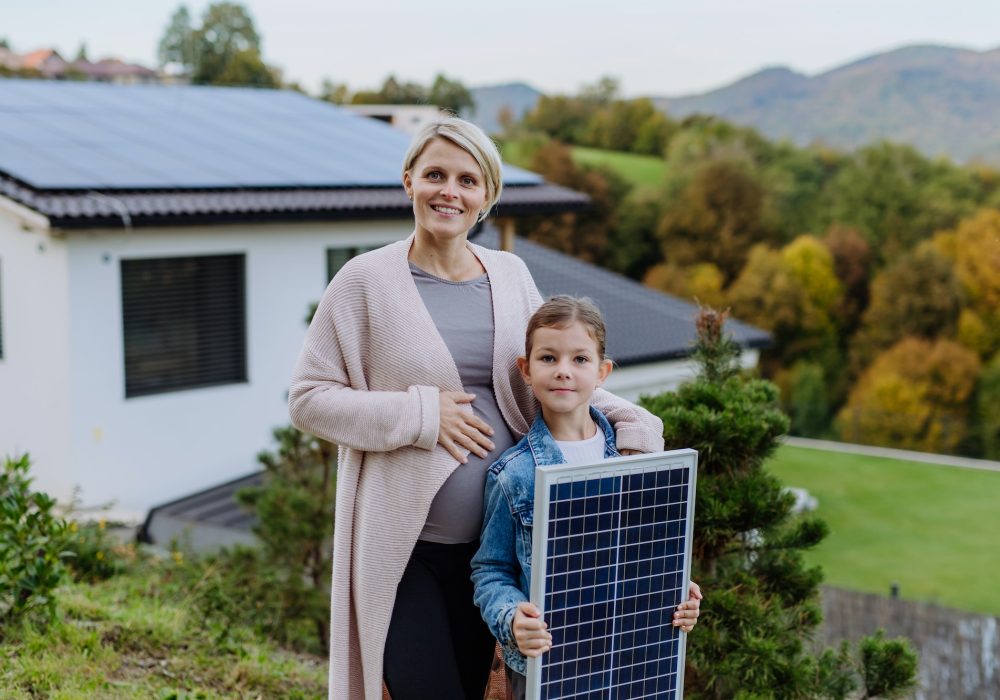 Mother with her little daughter near their house with solar panels. Alternative energy, saving